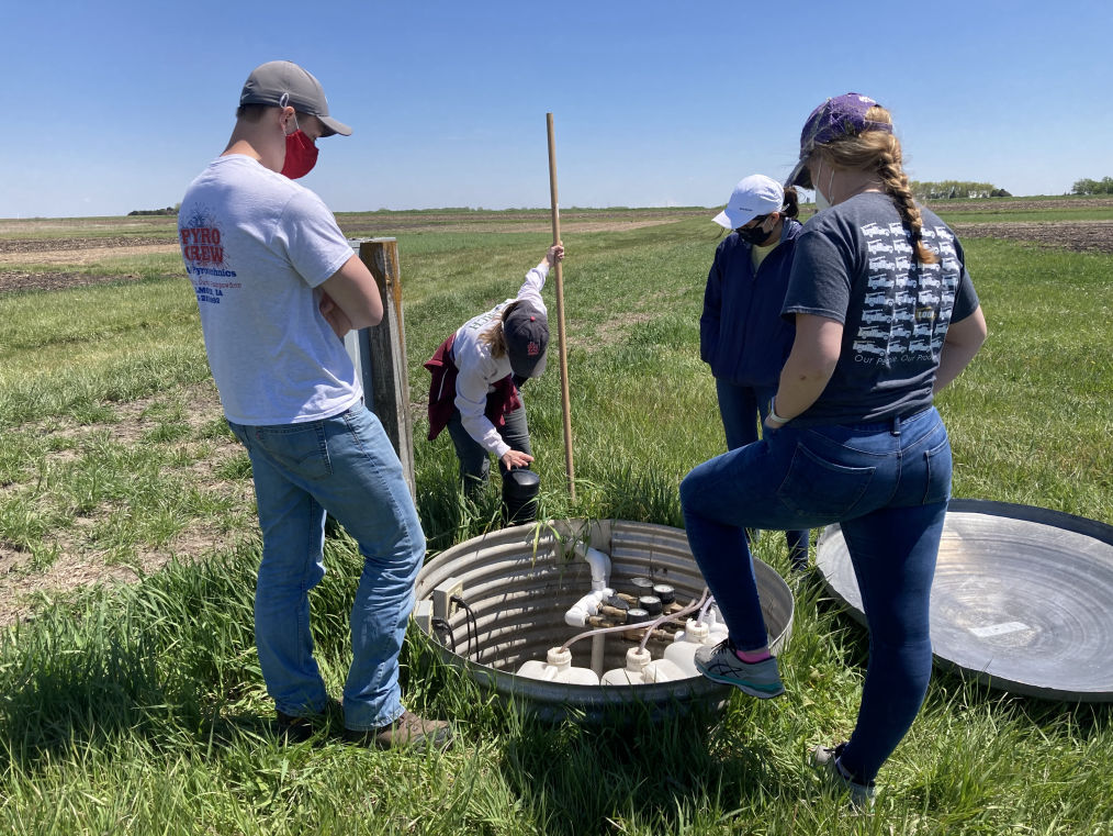 Four students stand around water collection sump in Gilmore City, IA.